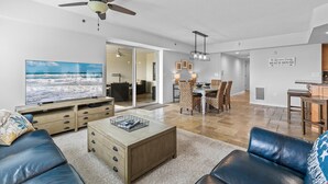 A spacious living room with a large flat-screen TV, a ceiling fan, and a dining area with chairs and a table. - Oceanwalk 10-601 (New Smyrna Beach)