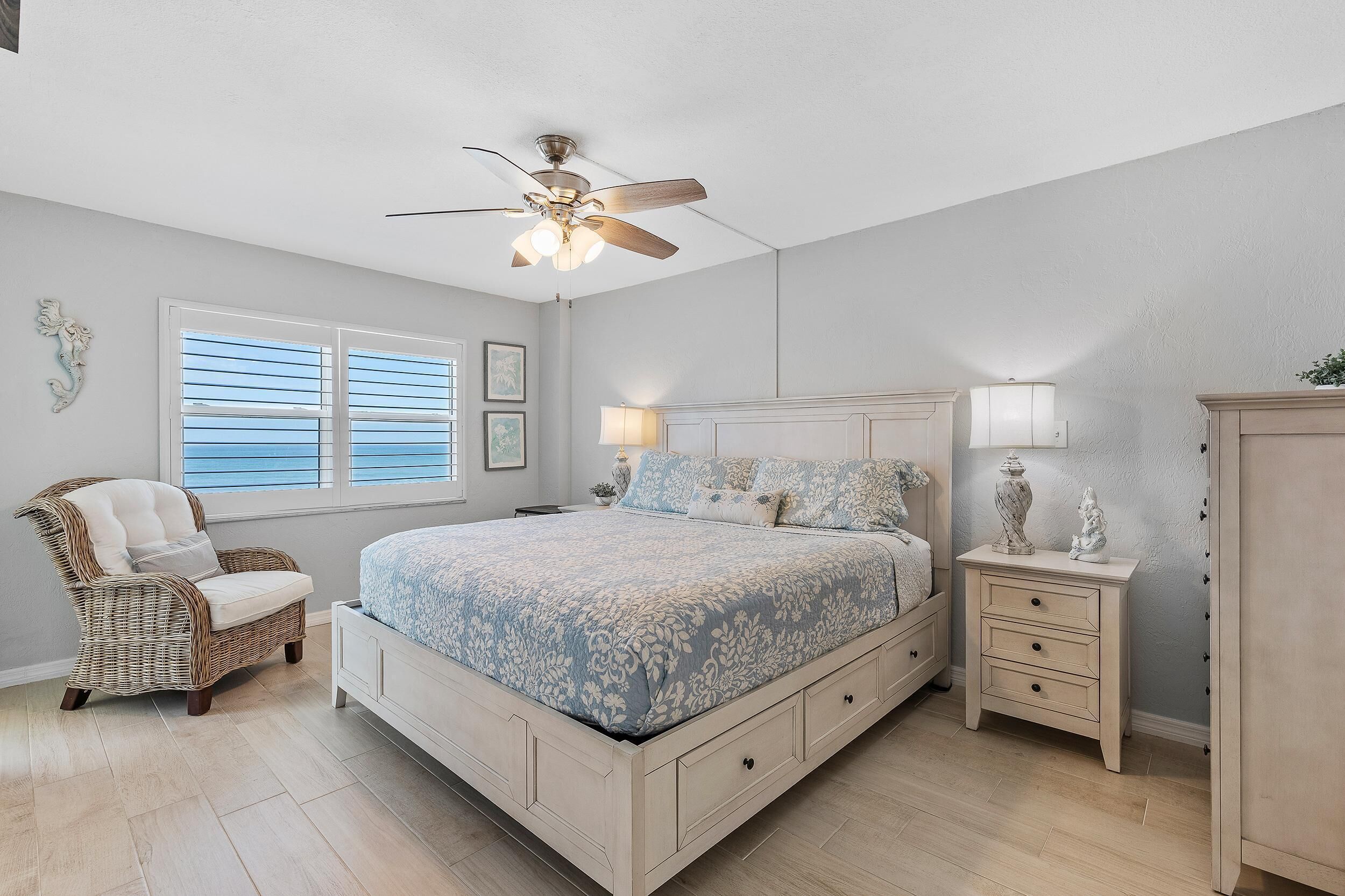 A bedroom with a bed, a chair, a nightstand, and a ceiling fan.