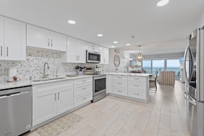 Enjoy meal preparation with a view of the ocean from this kitchen, featuring an oven, stainless steel appliances, and a large island with a sink and countertop.