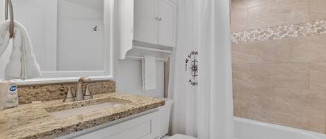 A bathroom with a granite countertop sink, a white toilet, and a bathtub.