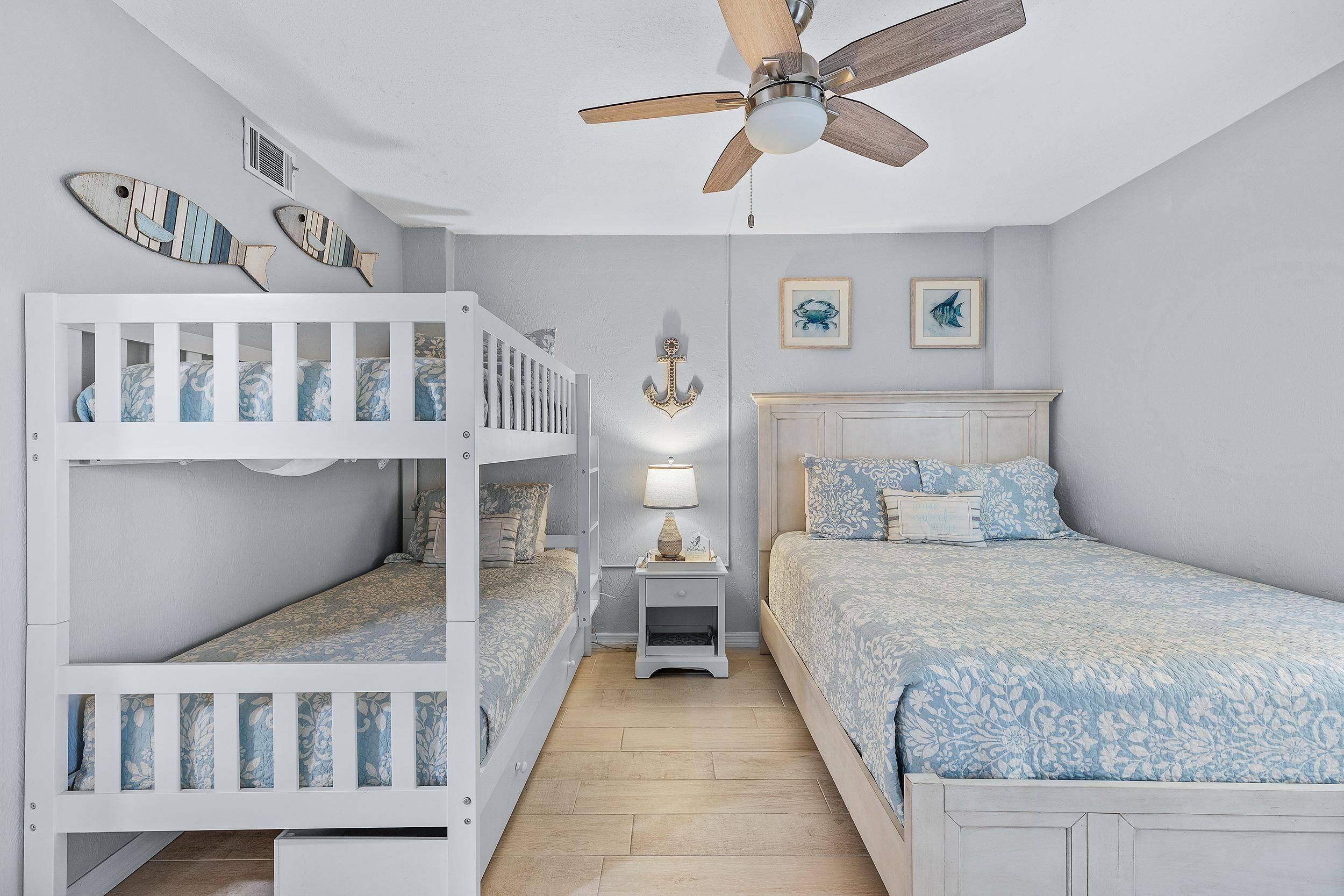 A child's room with bunk beds, a ceiling fan, and nautical-themed wall art.