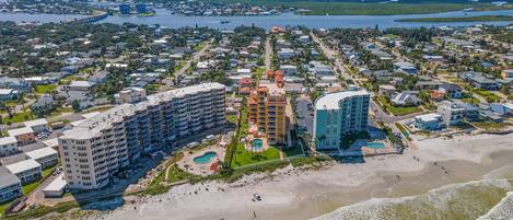 A coastal cityscape with a prominent hotel featuring multiple floors, a swimming pool, and beachfront access.