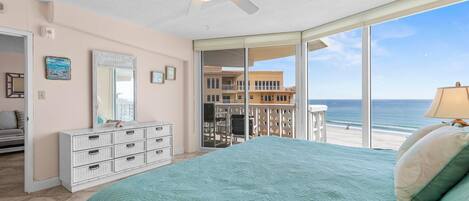Une chambre avec un grand lit, un ventilateur de plafond, une commode et une vue sur la plage.
