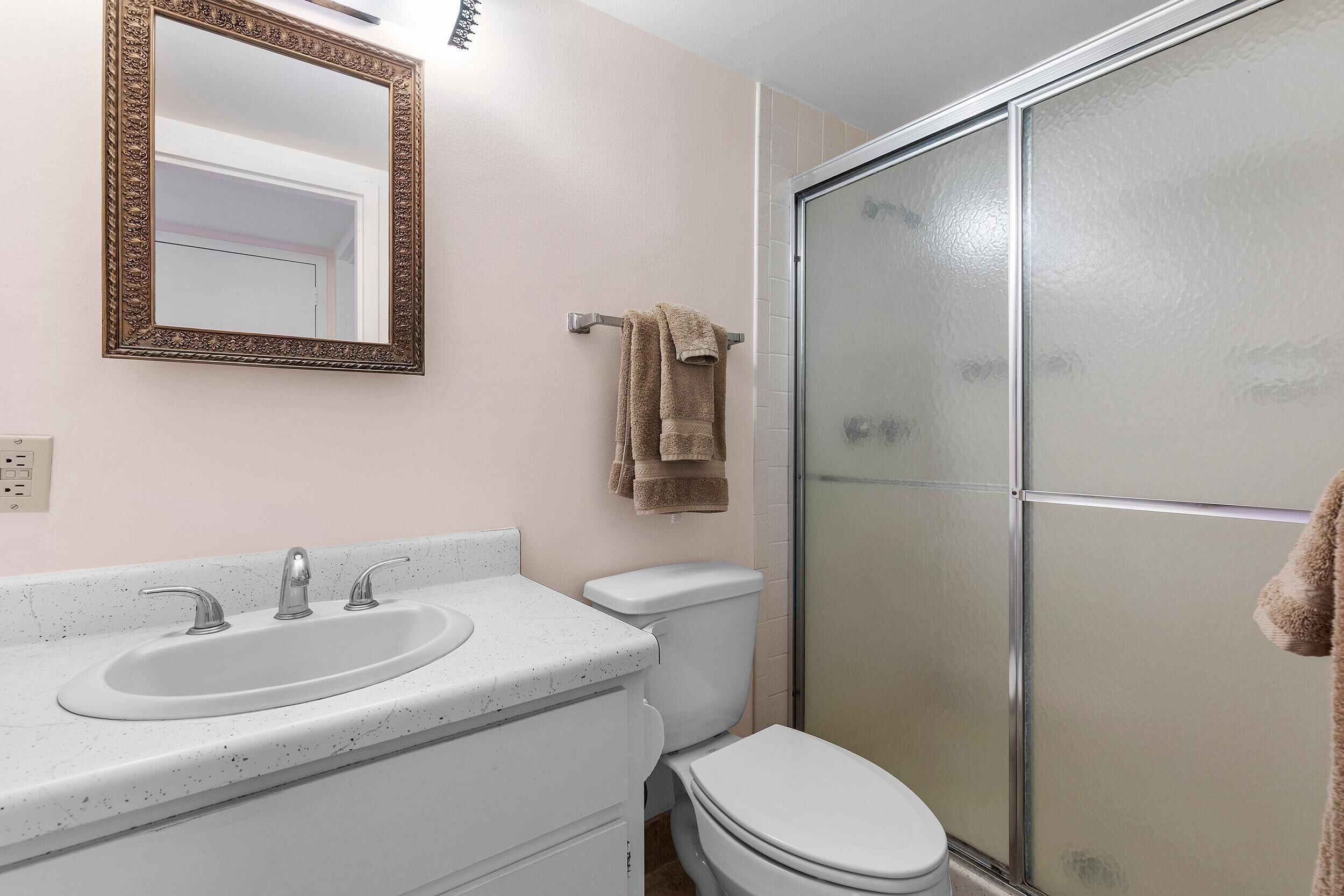 Un baño con lavamanos, espejo, inodoro y cabina de ducha de vidrio.