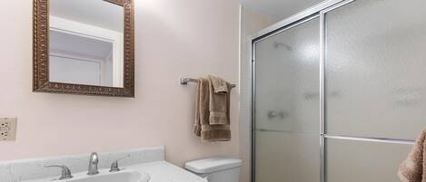 Un baño con lavamanos, espejo, inodoro y cabina de ducha de vidrio.