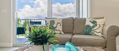 A living room with a sofa, a potted plant, and a tray with a glass and a white object.