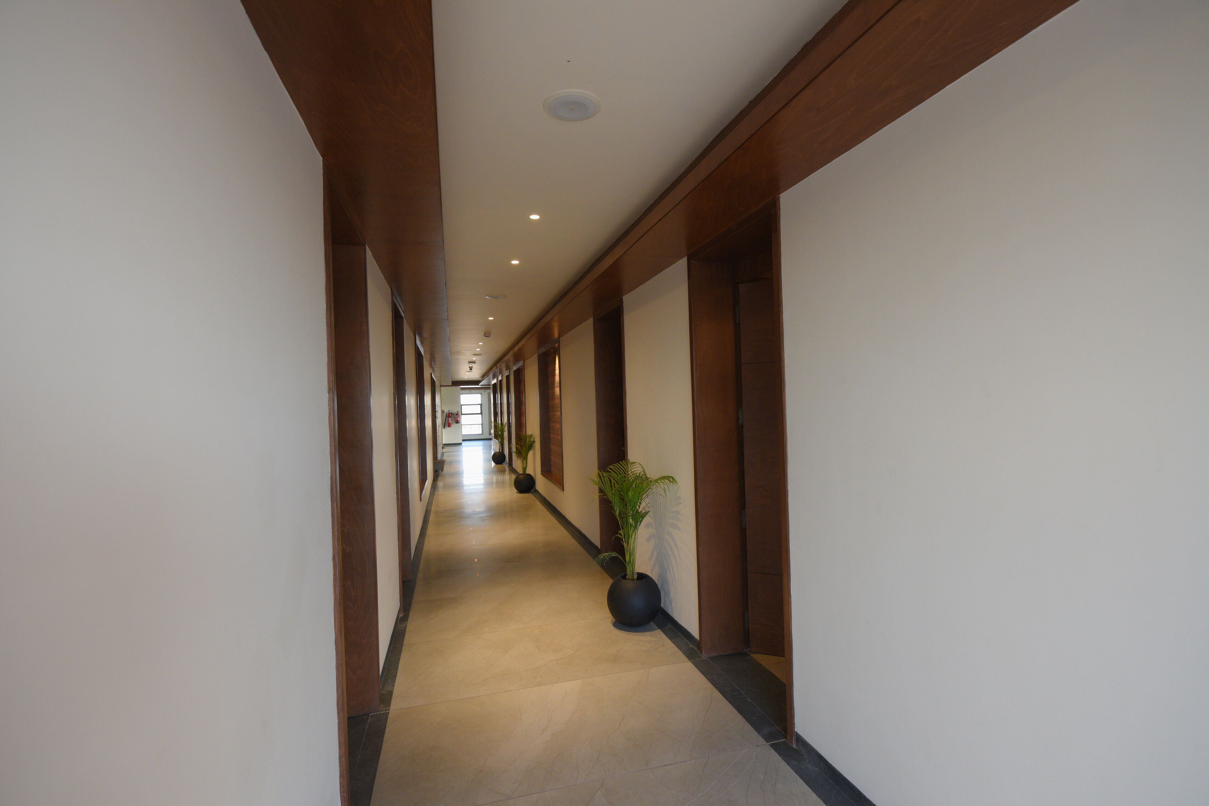 Un pasillo largo y estrecho con paneles de madera y suelo de baldosas, que conduce a una habitación luminosa al final.