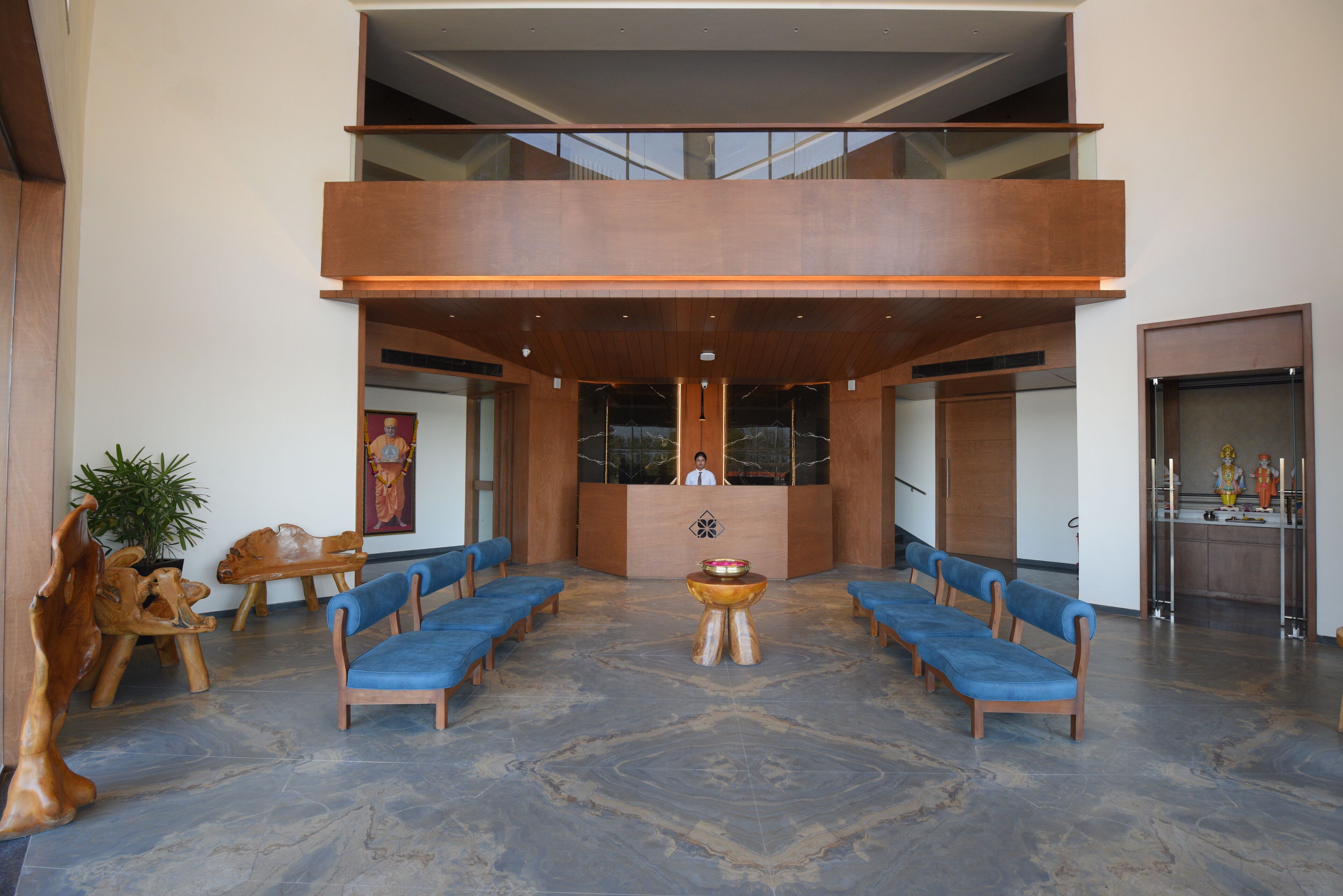 Een ruime lobby met een hoge plafond, een receptiebalie en een zithoek met blauwe stoelen.