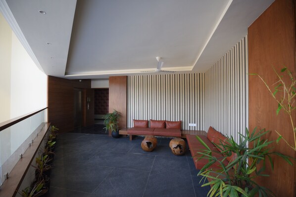 A modern interior with a dark tiled floor, a red sofa, and a ceiling fan. - Hotel The Pramukh by Shivalaya Darshanam (Sinor)