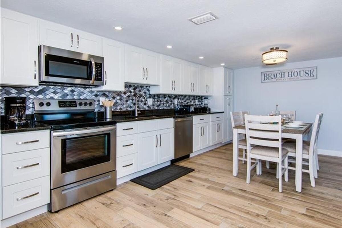 A modern kitchen with white cabinets, stainless steel appliances, and a dining area with a table and chairs.