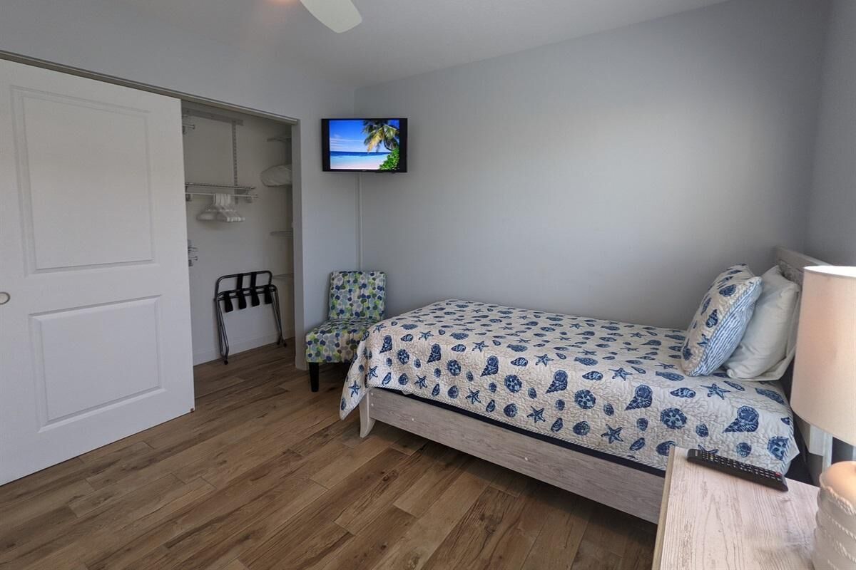 A bedroom with a bed, a TV mounted on the wall, a chair, and a door.
