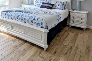 Une chambre à coucher avec un lit blanc, une literie à motifs floraux bleus, une table de chevet avec des tiroirs et un plancher en bois.