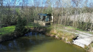 Un piccolo chalet di legno con tetto in metallo, immerso tra alberi e un piccolo stagno.