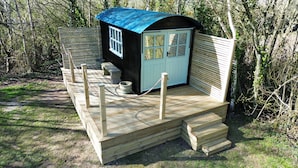 Una piccola casetta di legno con tetto blu, un portico con delle gradinate e una finestra.