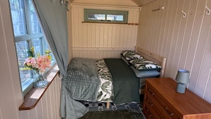 Una camera da letto compatta con un letto, una cassettiera, una finestra con tende e un tavolino con un vaso di fiori.
