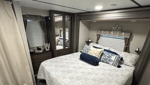 A bedroom with a large bed, a wardrobe, a mirror, and a window with curtains. - Charming RV Hideaway campground in Key Largo; Sun & Fun! (Key Largo)