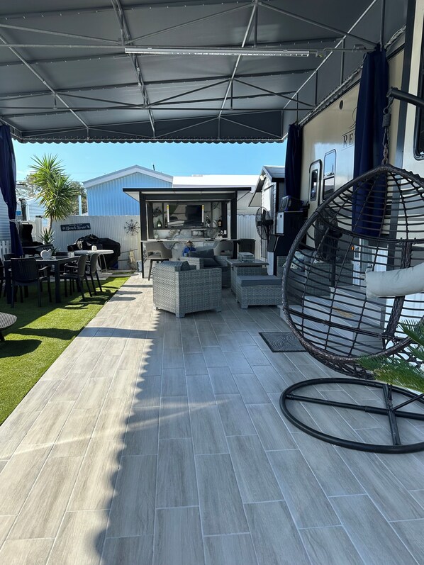 Un patio couvert aménagé avec du mobilier d’extérieur, un fauteuil suspendu et un barbecue.