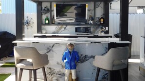 A modern outdoor kitchen with a marble countertop, two bar stools, a television, and various kitchen appliances. - Charming RV Hideaway campground in Key Largo; Sun & Fun! (Key Largo)