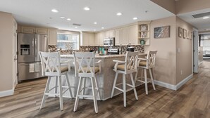 A modern kitchen with a central island, bar stools, stainless steel appliances, and a view to the outside. - Oceanwalk 1-401 (New Smyrna Beach)