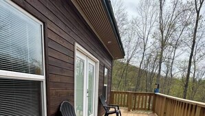 A wooden deck with two Adirondack chairs, a wooden railing, and a view of trees in the background. - Glenville’s Rustic Charm (Glenville)