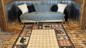 A cozy room with a wooden wall, a metal-framed window, and a checkered rug with animal prints. - Glenville’s Rustic Charm (Glenville)