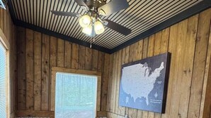 A rustic cabin interior with a wooden dining table, chairs, a ceiling fan, a window with blinds, and a map on the wall. - Glenville’s Rustic Charm (Glenville)