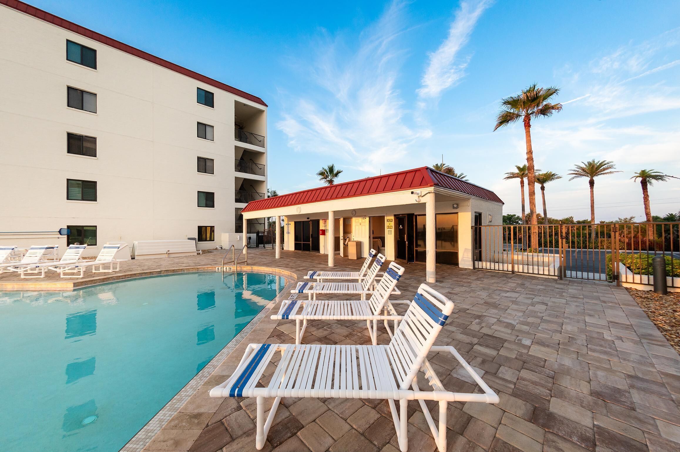 A pool area with lounge chairs and a building with multiple floors and balconies.
