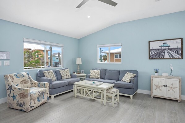 A living room with a blue sofa set, a patterned armchair, a white coffee table, and a starfish cabinet. - Upper Deck (Fort Myers Beach)