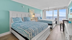 A bedroom with two beds, a desk, and a balcony with a view.