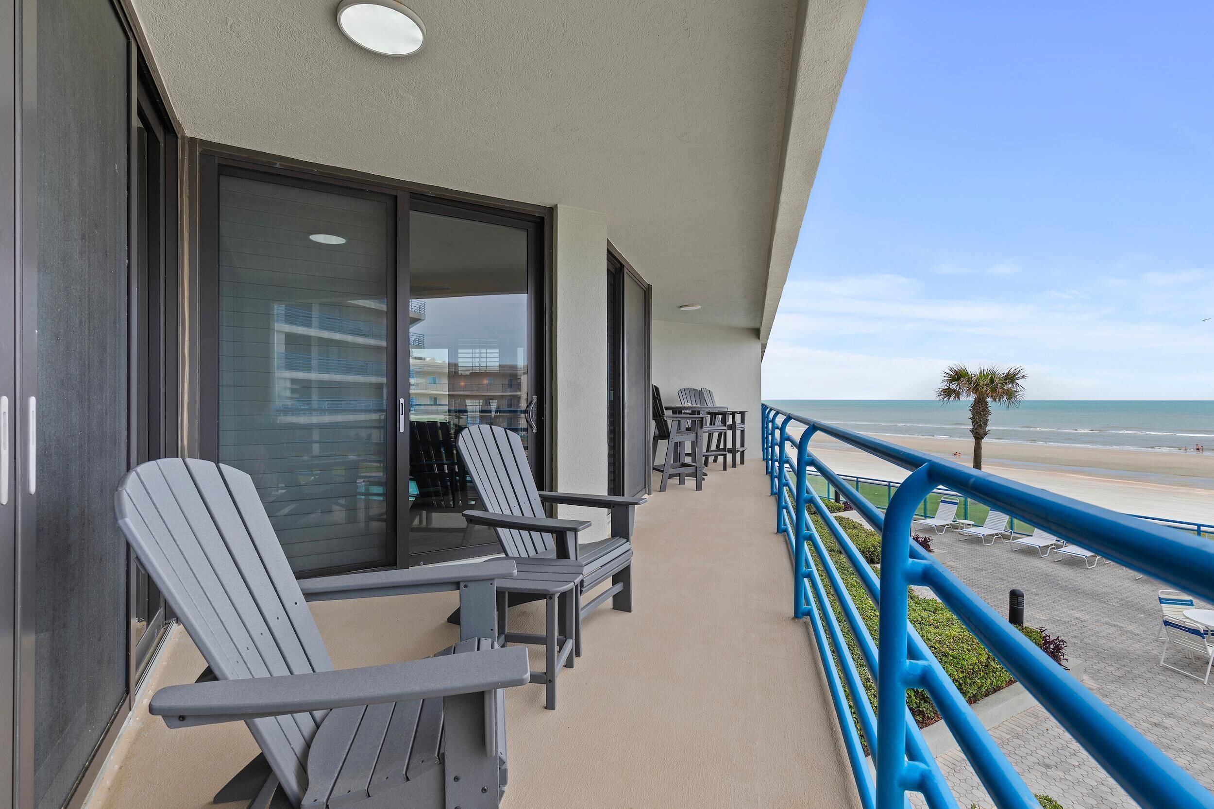 A balcony with Adirondack chairs, a table, and a view of the beach.