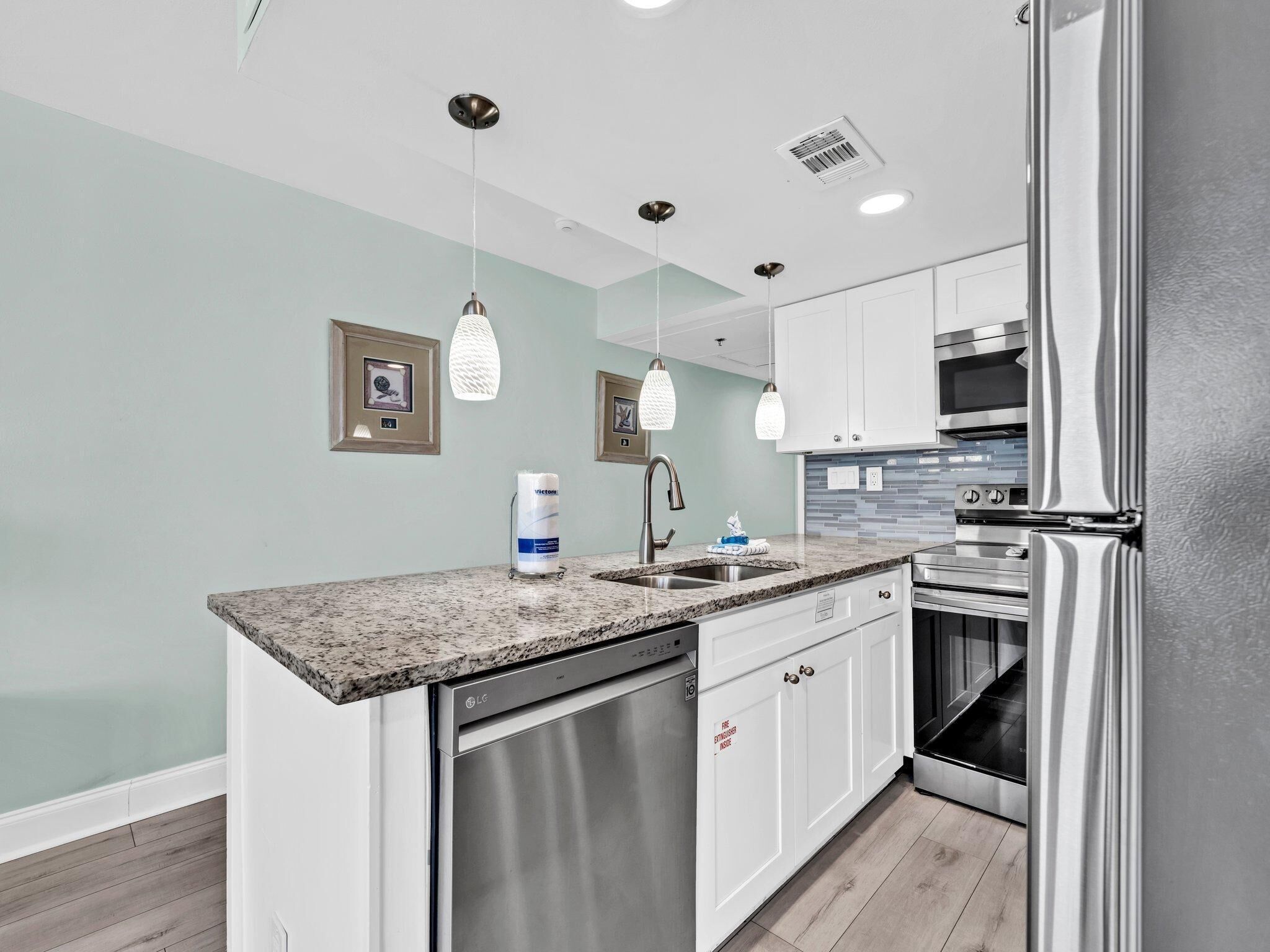 A modern kitchen with stainless steel appliances, white cabinetry, granite countertops, and pendant lighting.