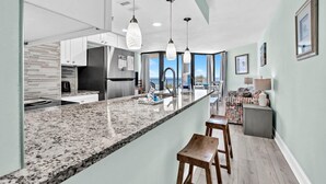 A modern kitchen with granite countertops, stainless steel appliances, and pendant lighting. - Sunbird 309e (Panama City Beach)