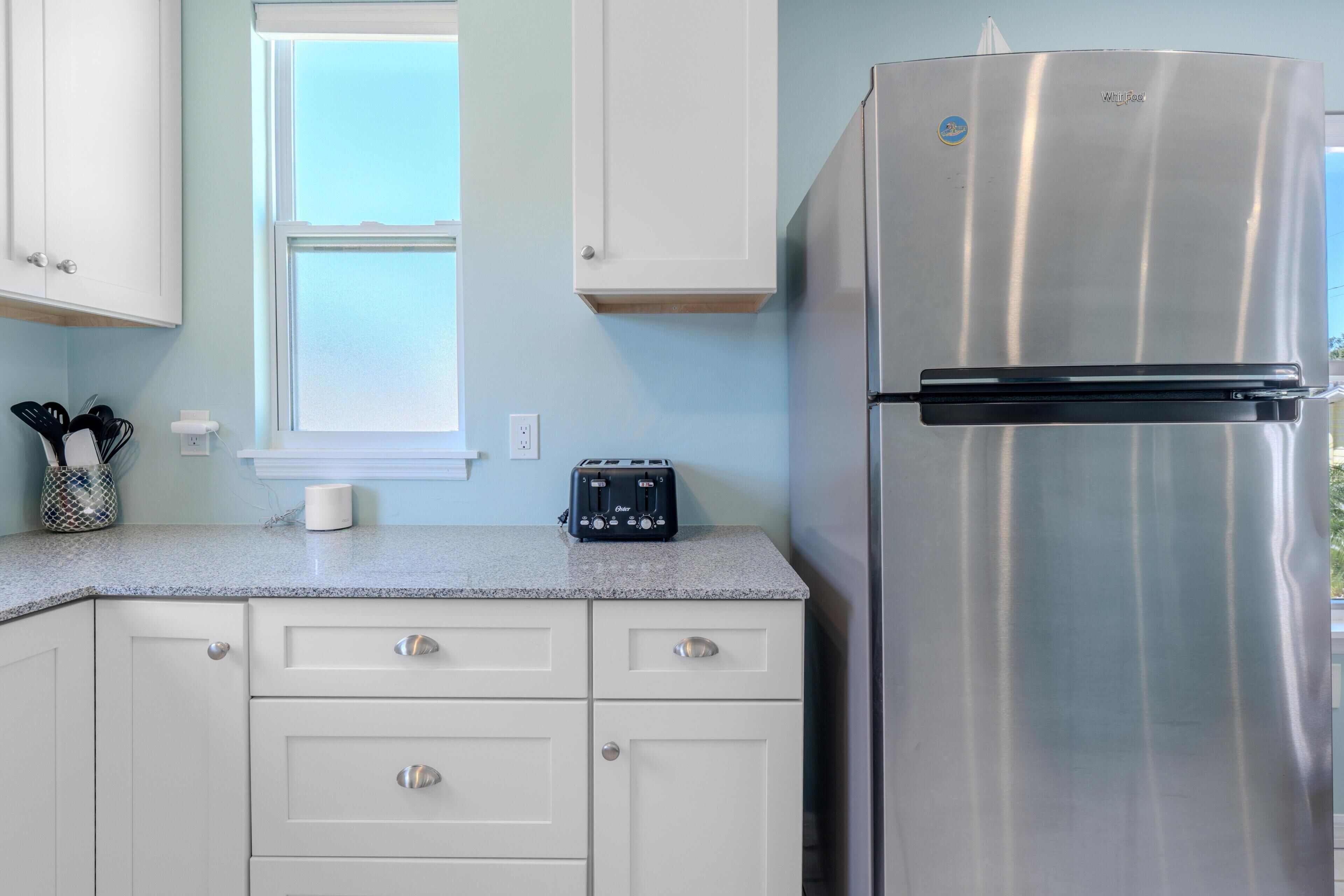 A kitchen with white cabinets, a stainless steel refrigerator, a toaster, and a window above the sink.
