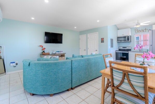 A living room with a sofa set, a television, and a kitchen area with a microwave.