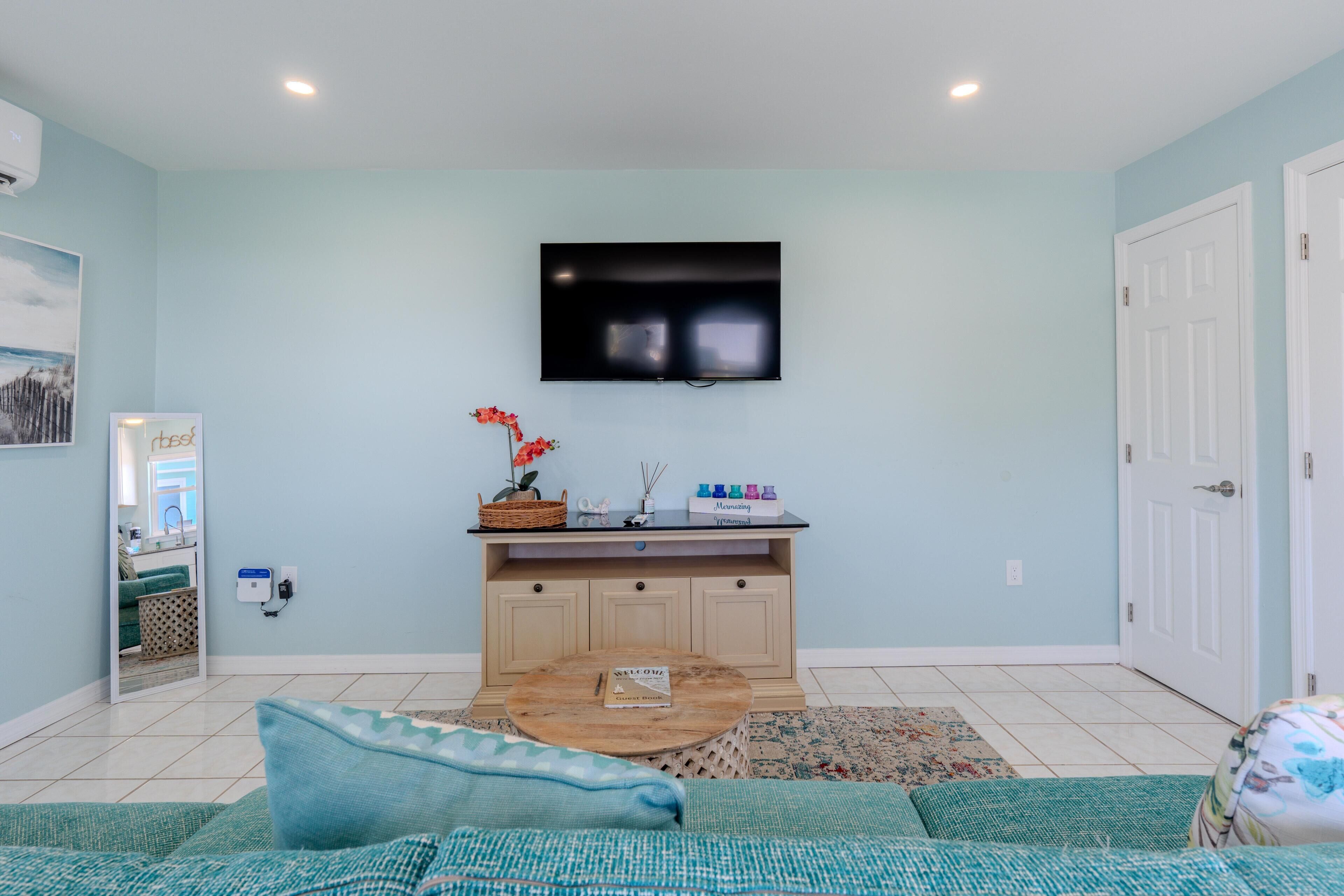 A living room with a flat-screen TV mounted on the wall, a sofa, a coffee table, and a door.