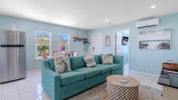 A modern living room with a teal sofa, a round coffee table, and a kitchen area with a refrigerator.