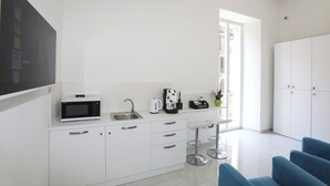 A modern kitchen with a microwave, sink, and bar stools. There is a cabinet with drawers and a large white cabinet to the right. - VivimiHome - CharmiNaples (Naples)