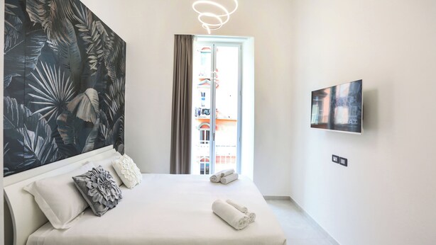 A modern hotel room with a large bed, a wall-mounted TV, and a view of the outside balcony. - VivimiHome - CharmiNaples (Naples)