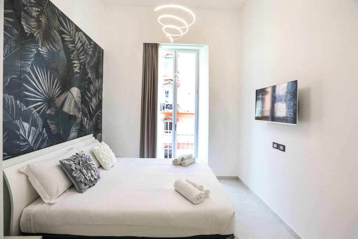 A modern hotel room with a large bed, a wall-mounted TV, and a view of the outside balcony.