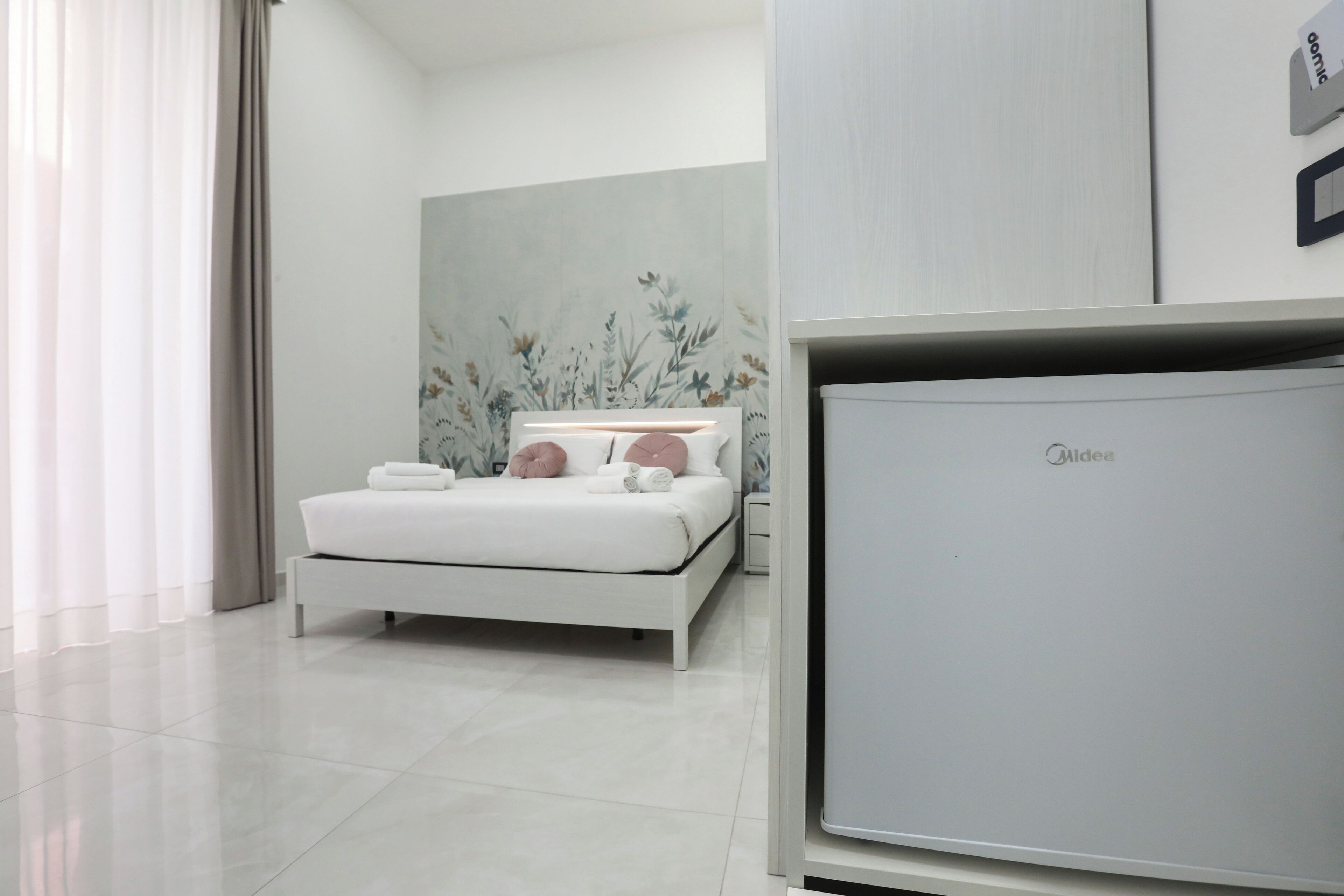 Un dormitorio moderno con una cama blanca, una mesita de noche y un televisor montado en la pared.