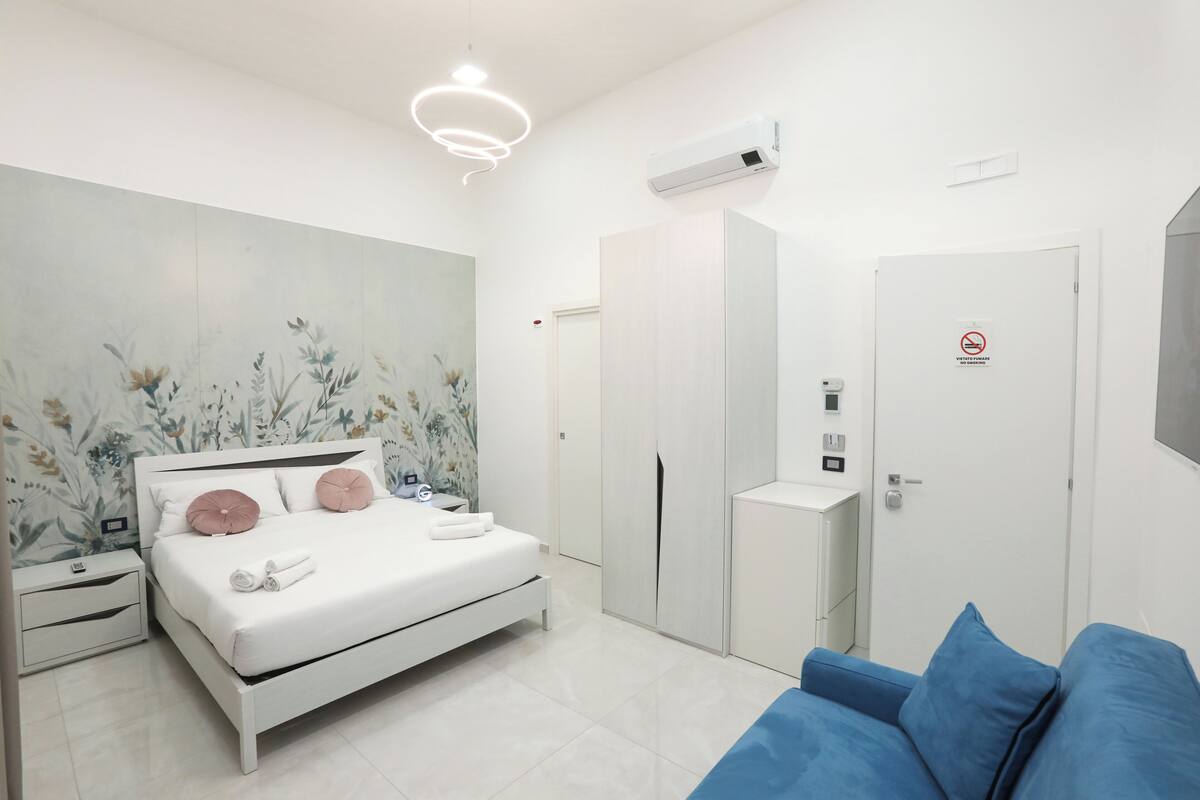 A modern bedroom with a bed, nightstands, a wardrobe, a blue sofa, and a wall-mounted air conditioner.