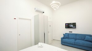 A modern hotel room with a white bed, a blue sofa, a flat-screen TV, and a ceiling light fixture. - VivimiHome - CharmiNaples (Naples)