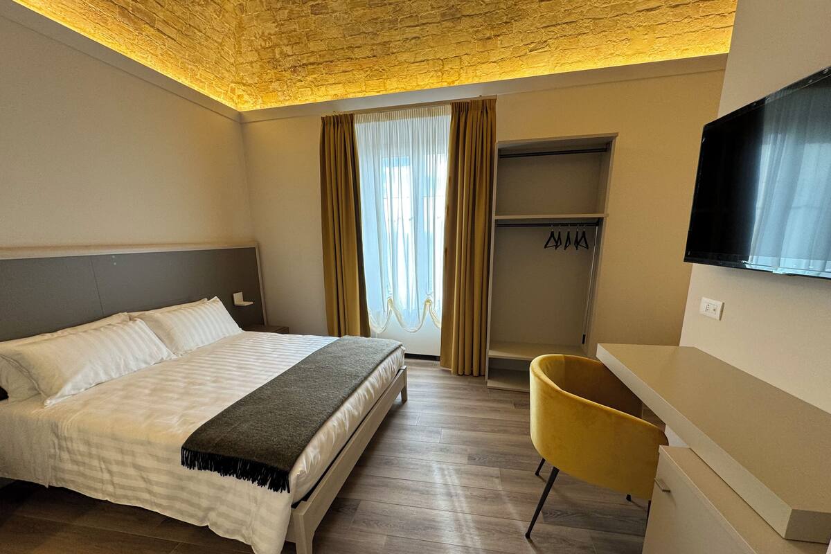 Ein Hotelzimmer mit Bett, Schreibtisch, Stuhl, Fernseher und Kleiderschrank.