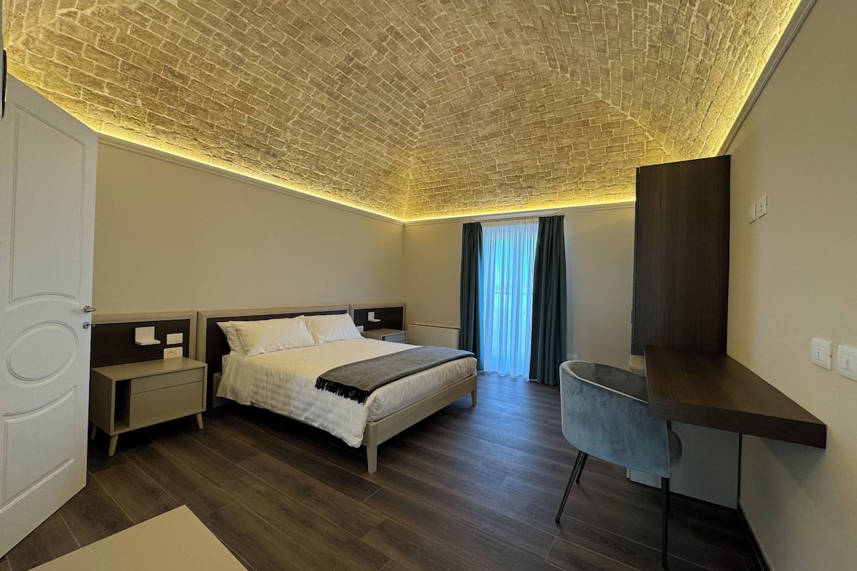Ein modernes Schlafzimmer mit Ziegelmuster-Decke, einem Bett, einem Schreibtisch und einem großen Fenster mit Vorhängen.