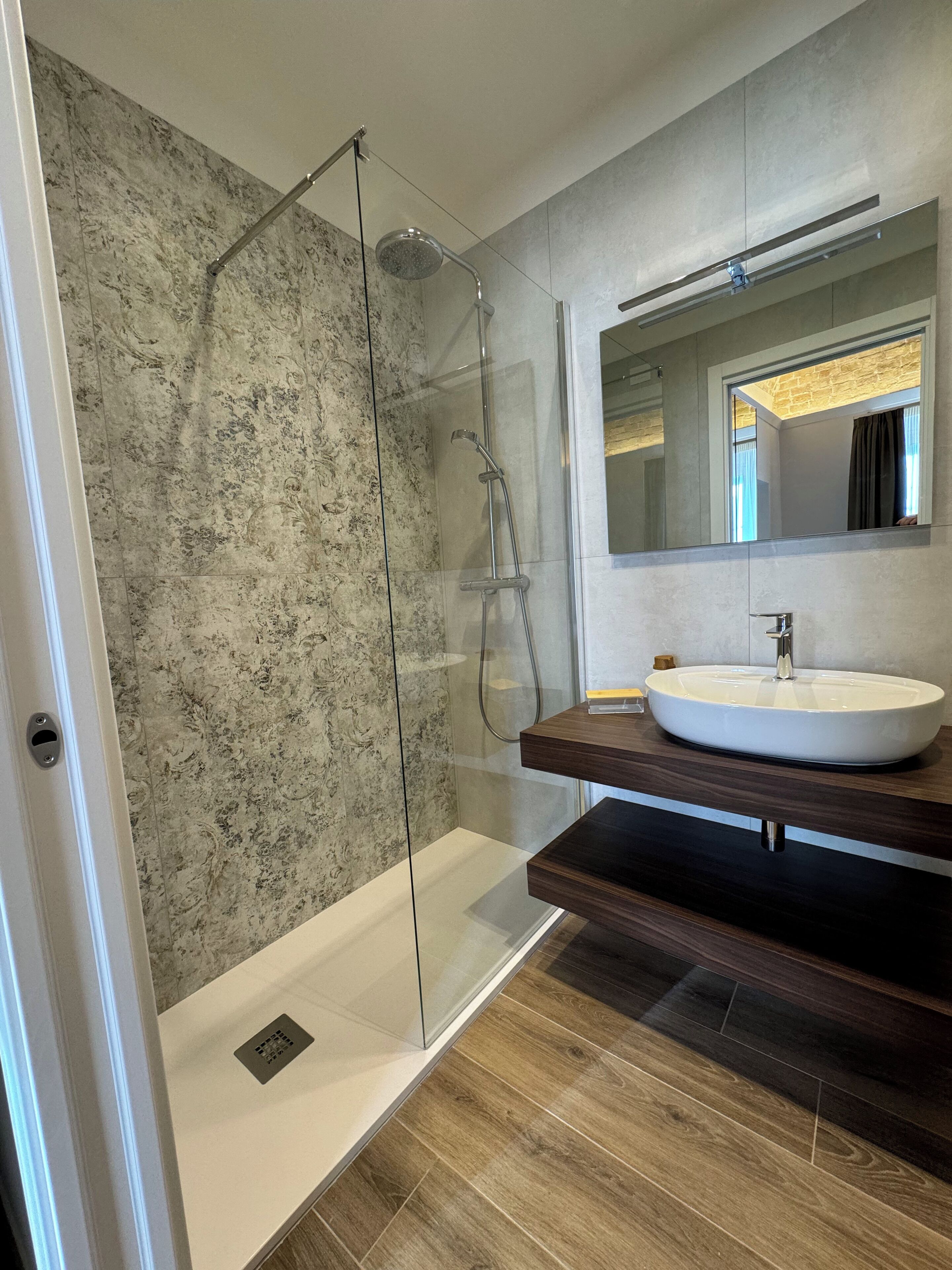 A modern bathroom with a glass-enclosed shower, a large mirror, and a wooden vanity with a sink.