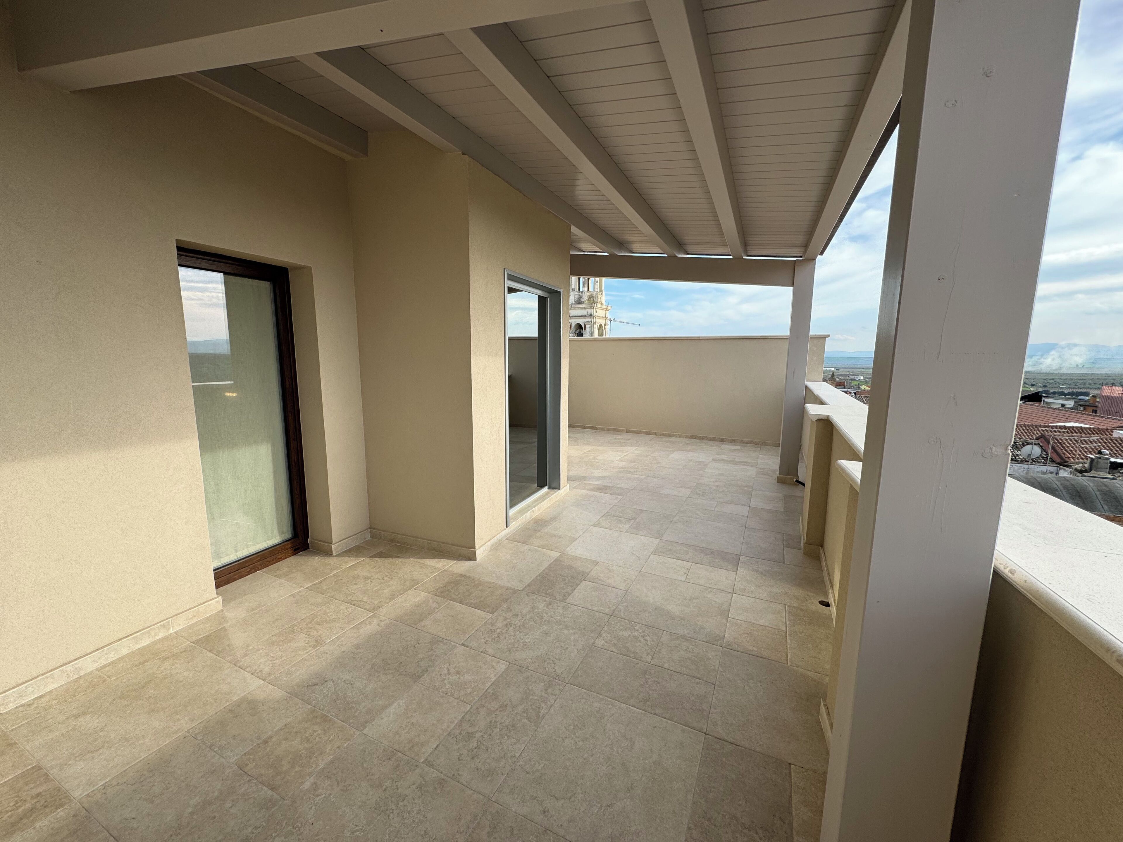 A balcony with a tiled floor, a glass door, and a view of a cityscape.