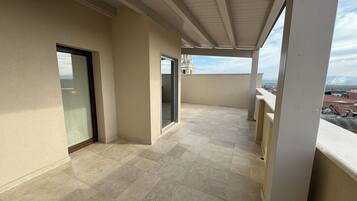 A balcony with a tiled floor, a glass door, and a view of a cityscape.