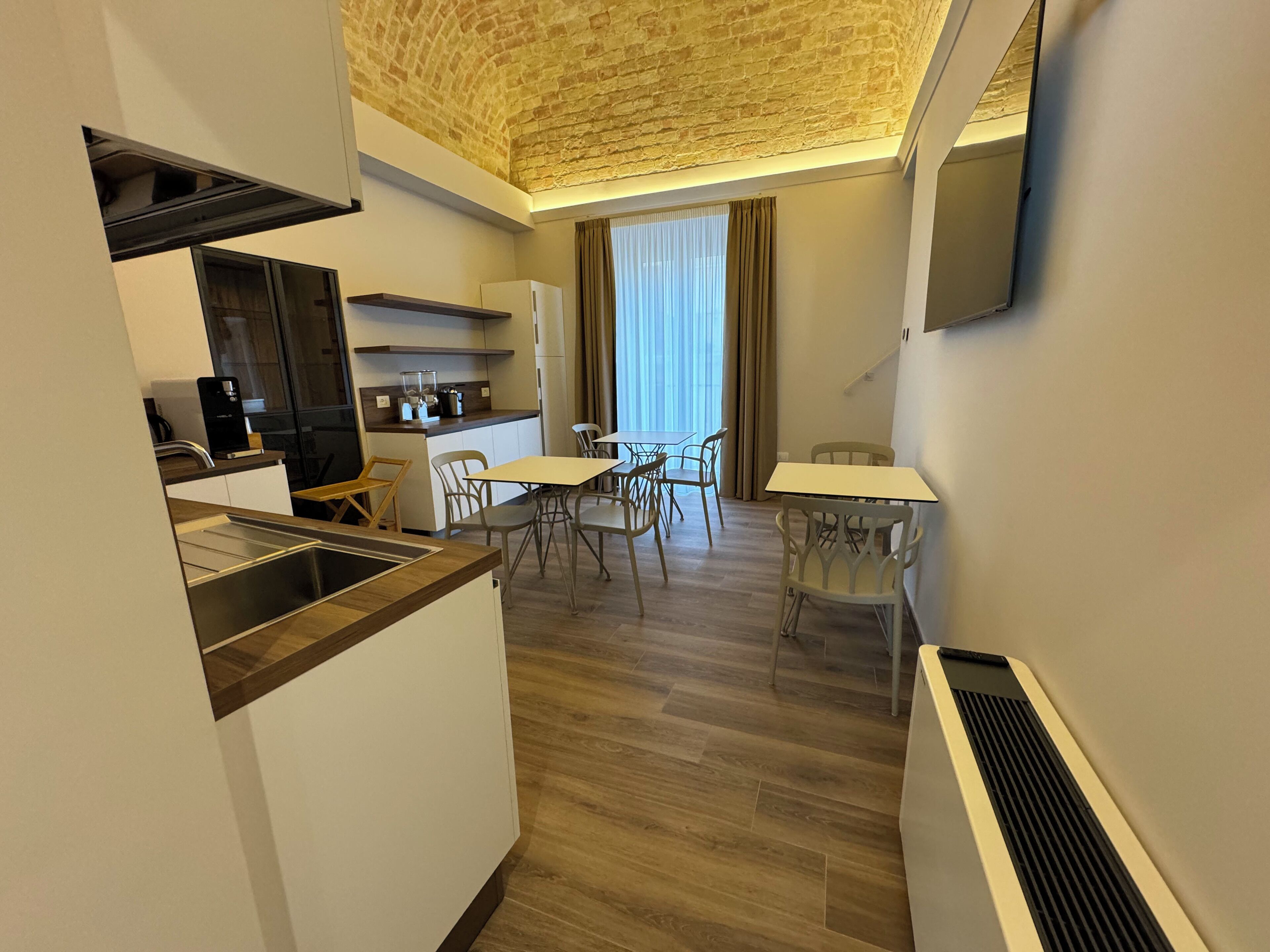 Une cuisine compacte dotée d’appareils électroménagers modernes, un coin repas avec une table et des chaises, et une grande fenêtre avec des rideaux.