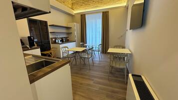 Une cuisine compacte dotée d’appareils électroménagers modernes, un coin repas avec une table et des chaises, et une grande fenêtre avec des rideaux.