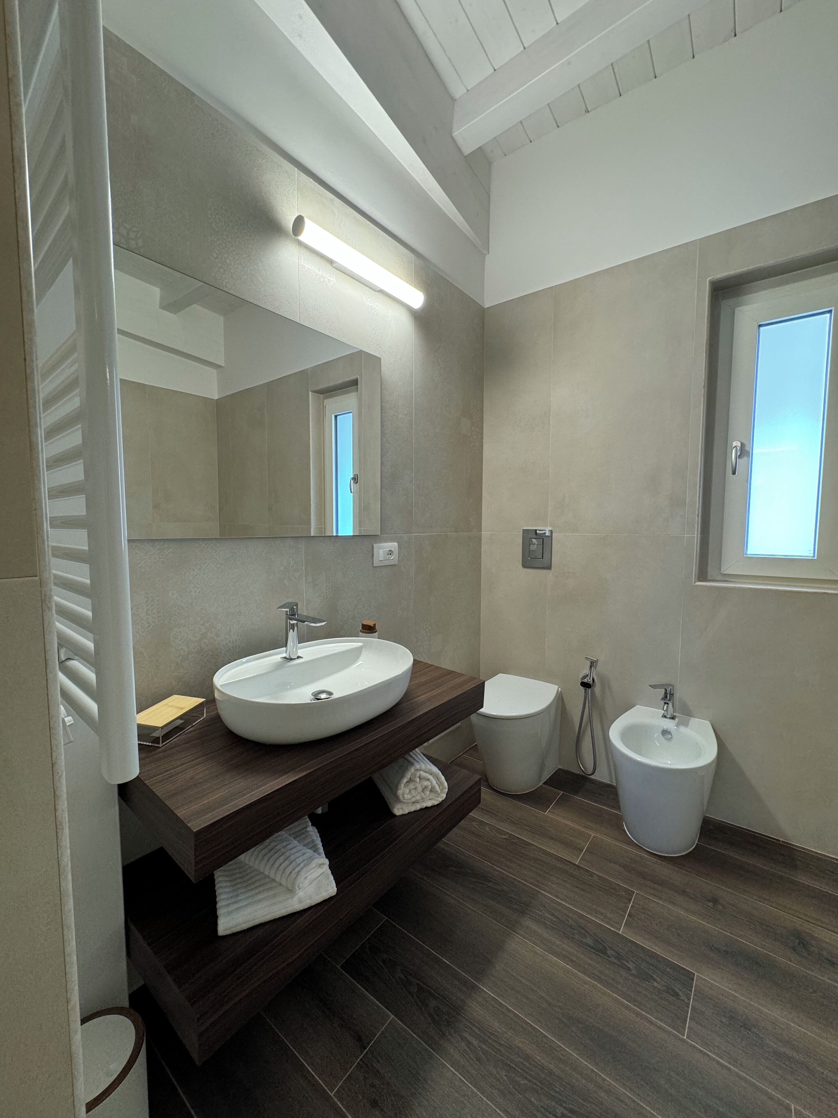 A modern bathroom with a large mirror, a round sink, a toilet, and a bidet.